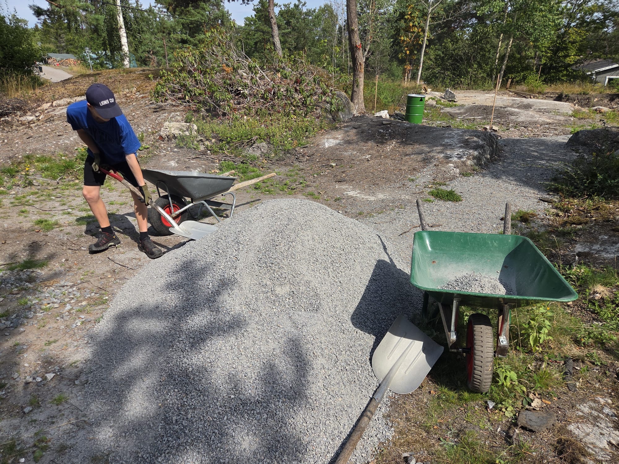 Ungdom skottar grus i skottkärra vid stuga